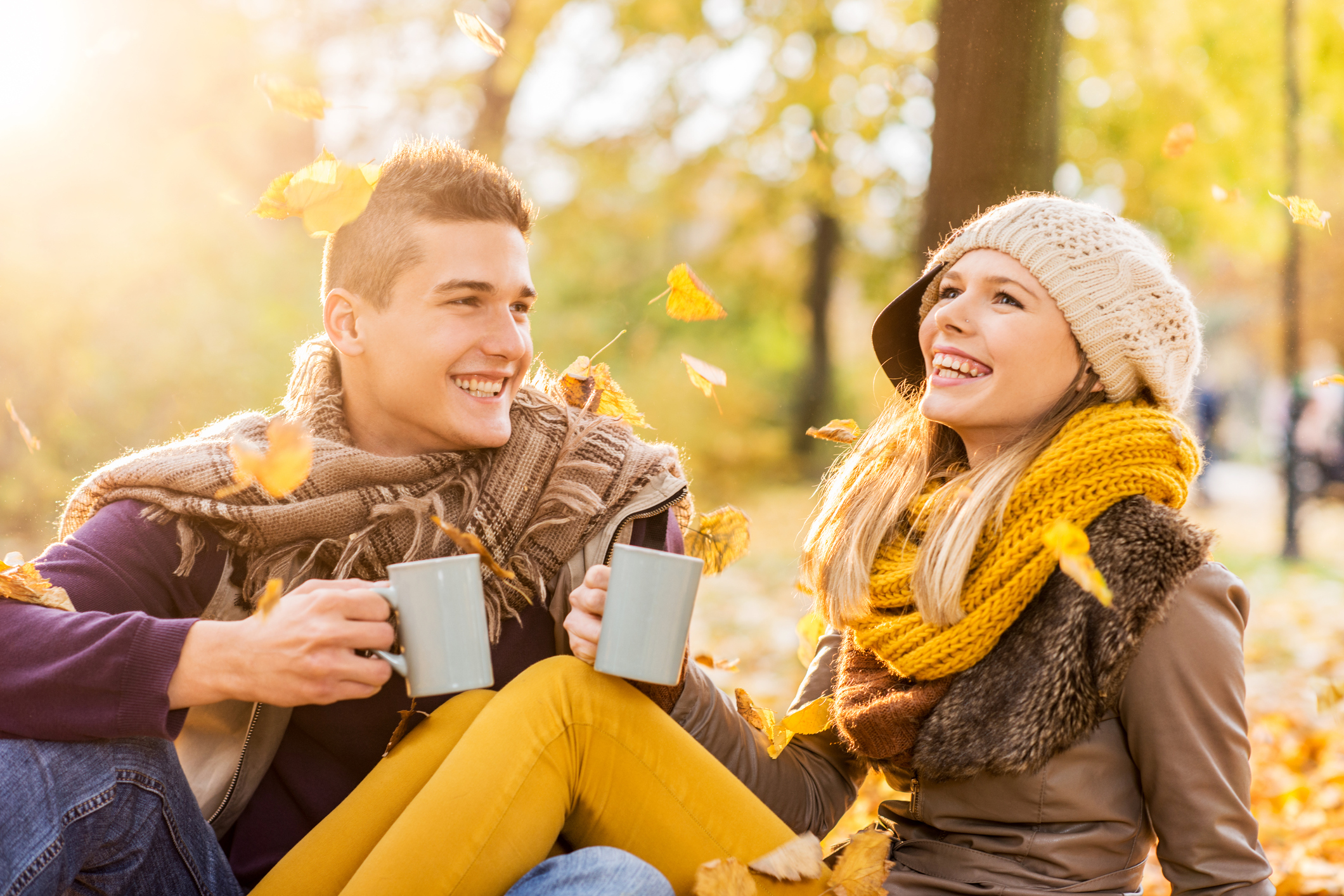 Happy teenage couple communicating and drinking coffee while sitting in park on a beautiful autumn day.  