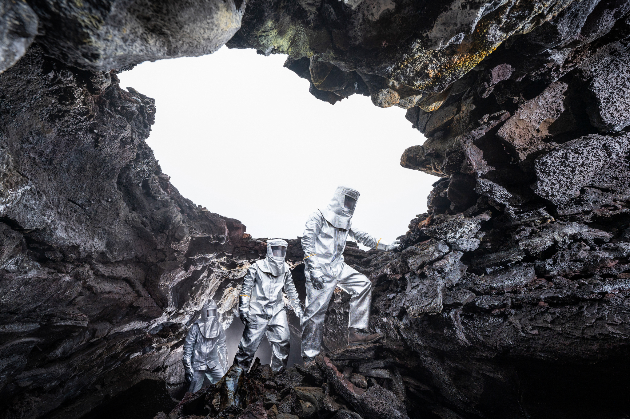 Expedition team members in heat-resistant suits climb into a fresh lava tube in southern Iceland in search of newly deposited minerals and the first microscopic signs of life. (Robbie Shone, National Geographic)