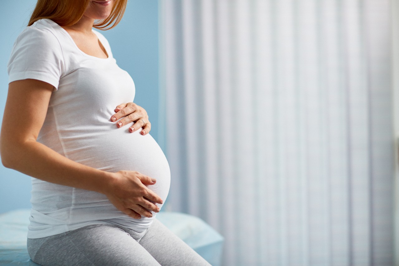 pregnant woman holding belly sitting on bed