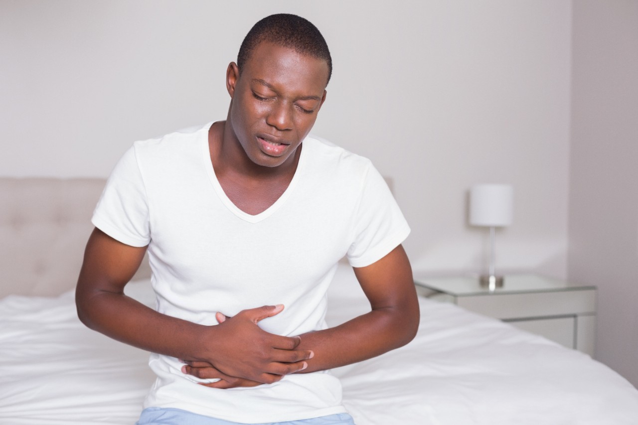 man sitting on bed holding stomach in pain