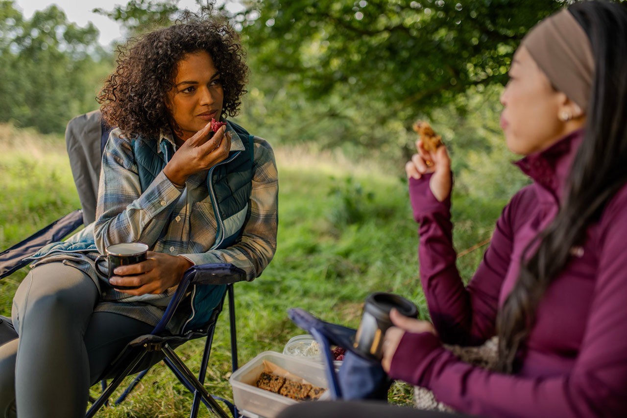 Two ladies sitting on folding chairs outside while snacking