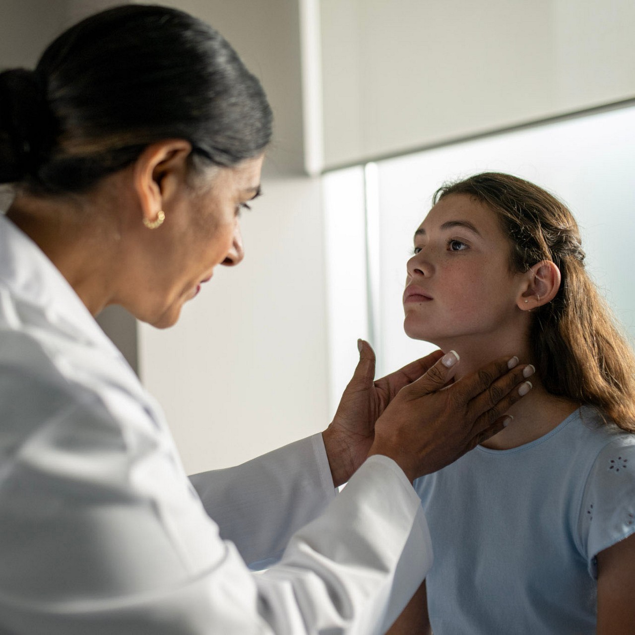 Una professionista sanitaria che valuta il collo di una paziente adolescente.